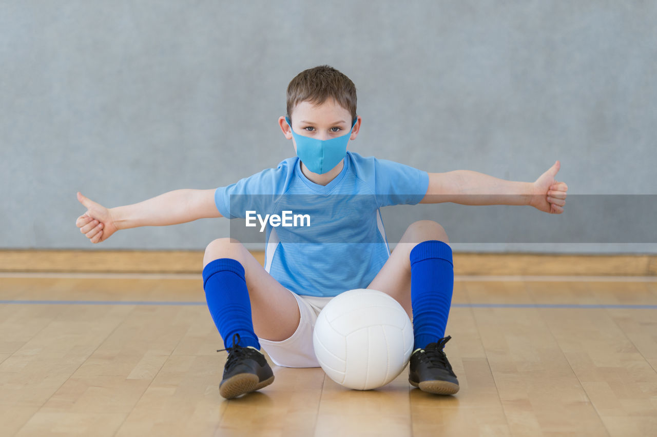 Portrait of boy wearing mask sitting on floor with volleyball