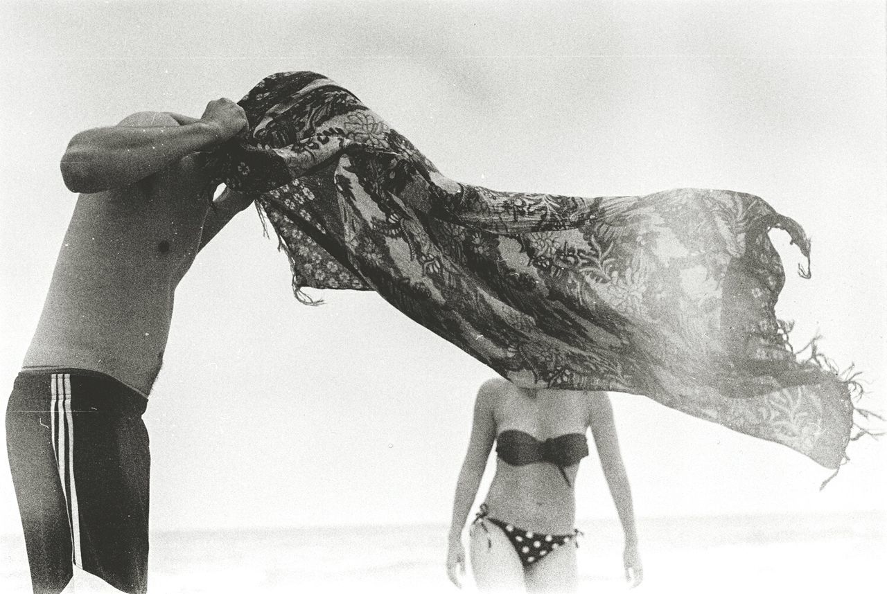 Midsection of people covering face with shawl on sunny day at beach