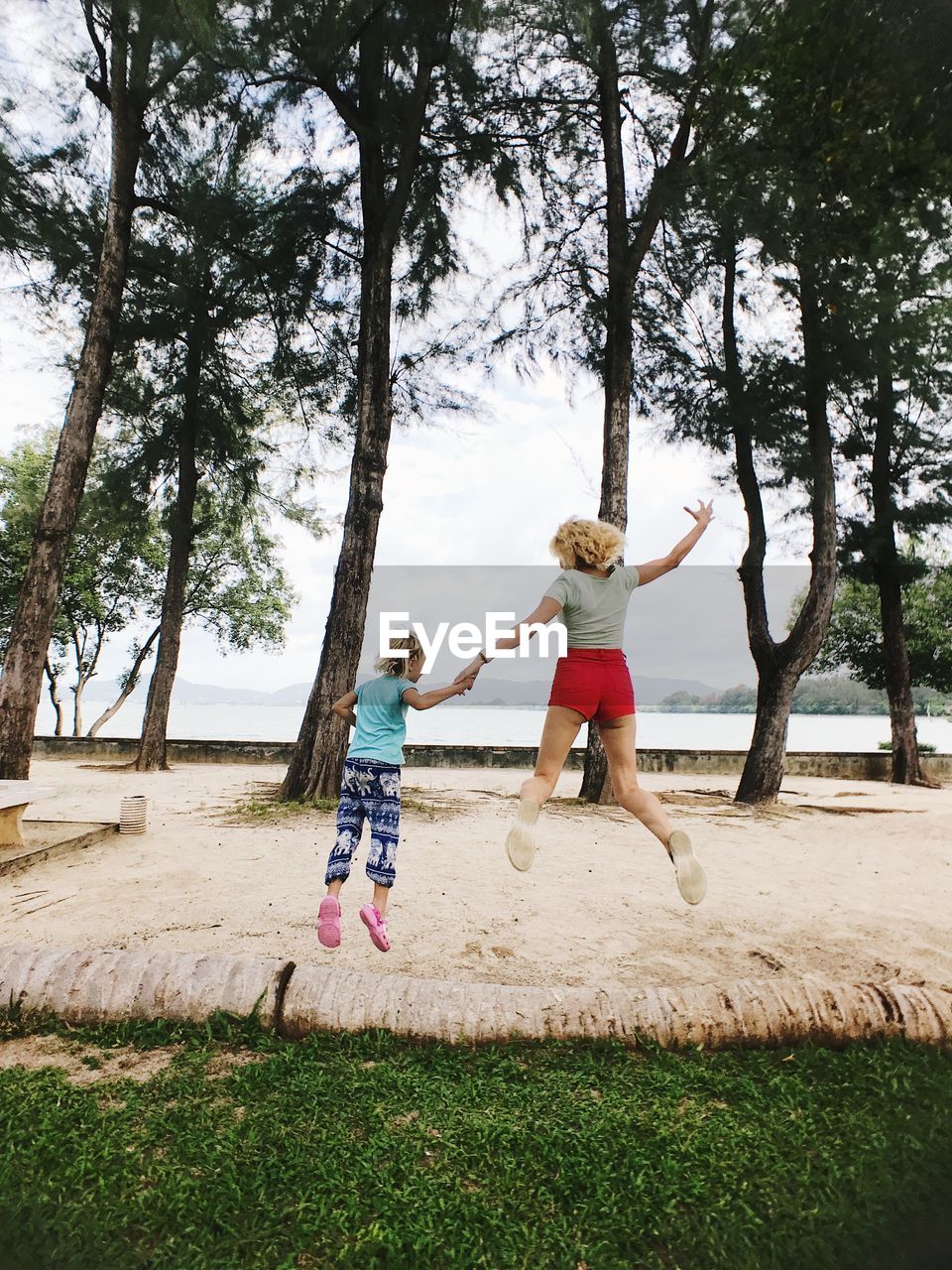 Full length rear view of woman and daughter jumping on sand