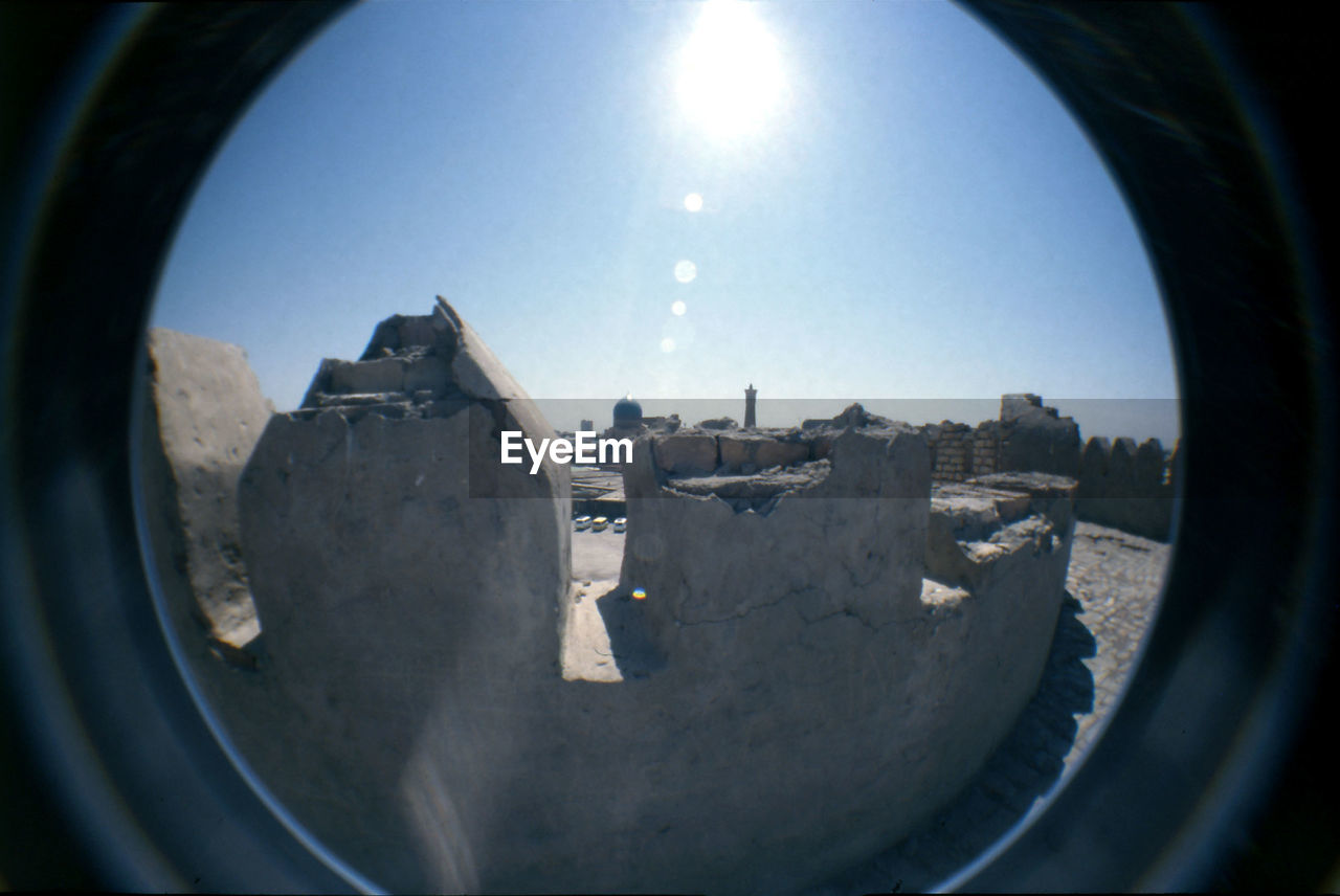 Ruined structure against blue sky on sunny day seen through glass