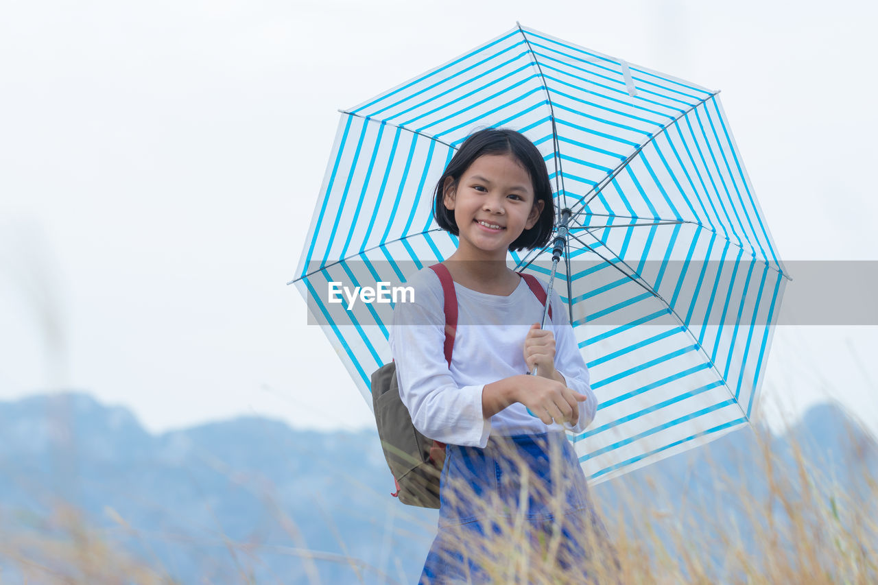Portrait of smiling girl with umbrella standing on field against sky