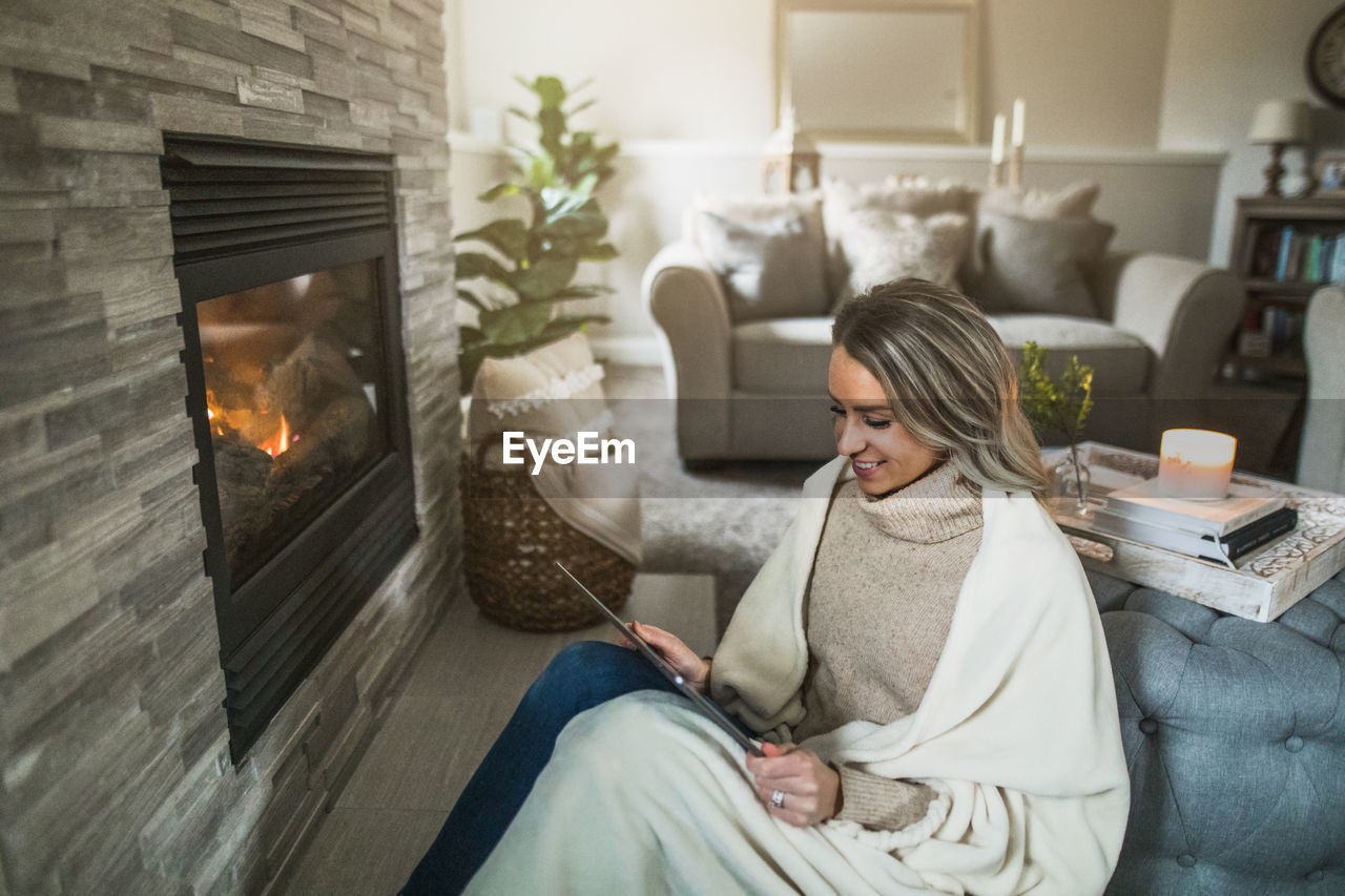 Smiling woman using digital tablet while sitting on sofa at home