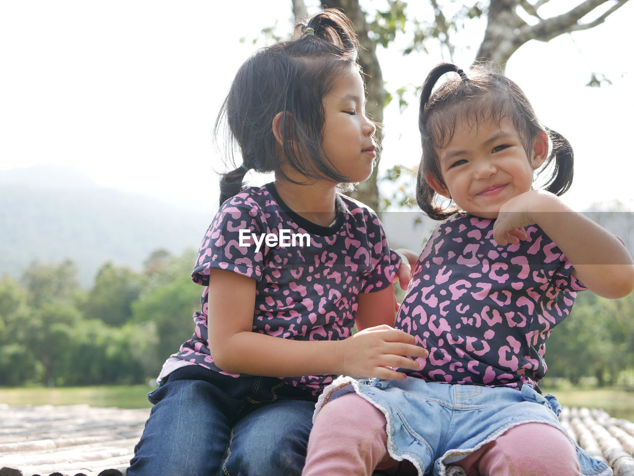 Cute girls playing at park while sitting against tree