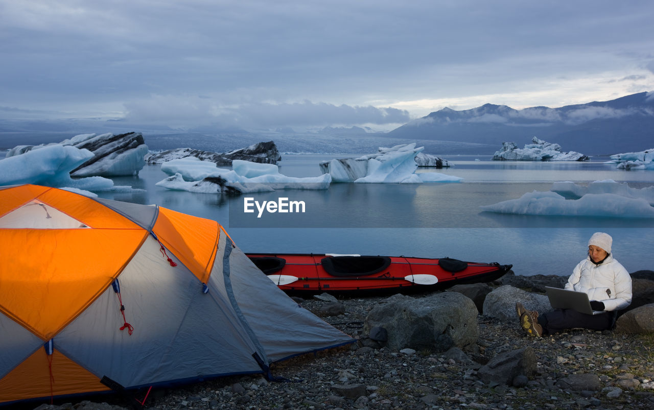 Woman using her laptop at campsite by glacier lagoon