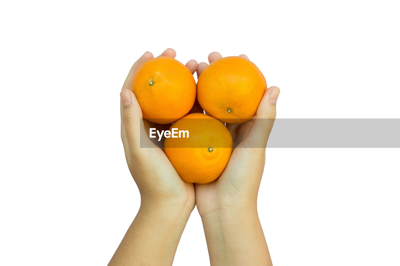 Close-up of hand holding orange against white background