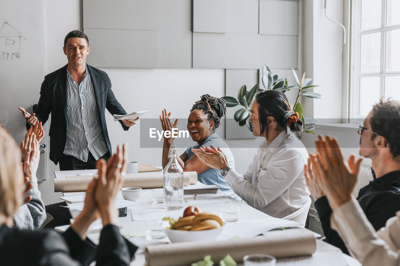 Male and female business people applauding for manager during meeting at work place