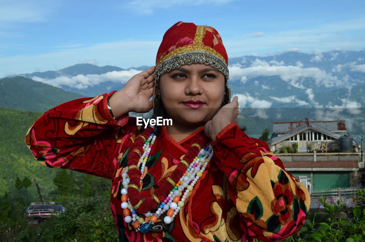 PORTRAIT OF SMILING YOUNG WOMAN AGAINST MOUNTAIN