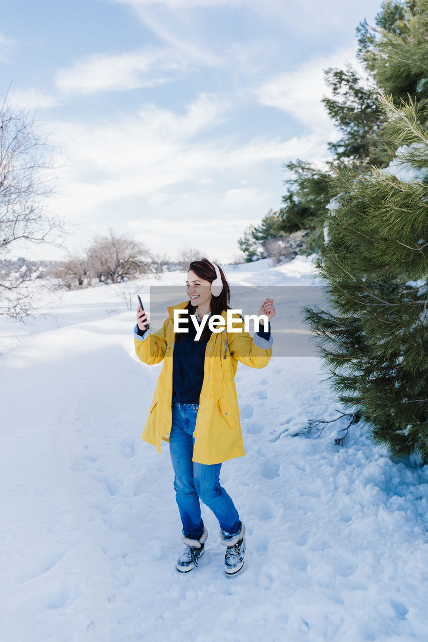 Young woman using phone while standing on snow