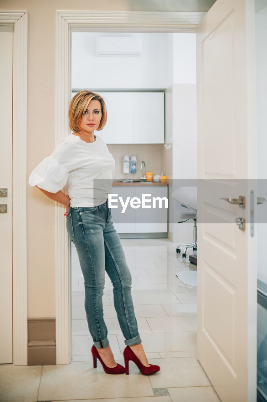 Portrait of a beautiful slender woman in full growth in the doorway of a bright medical office