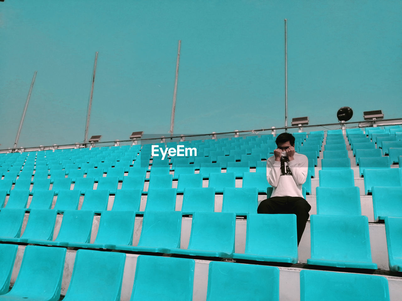 An unknown person sitting on blue seat at stadium 