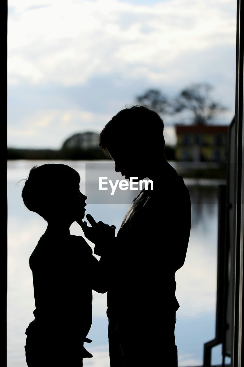 Side view of silhouette siblings standing by door at home