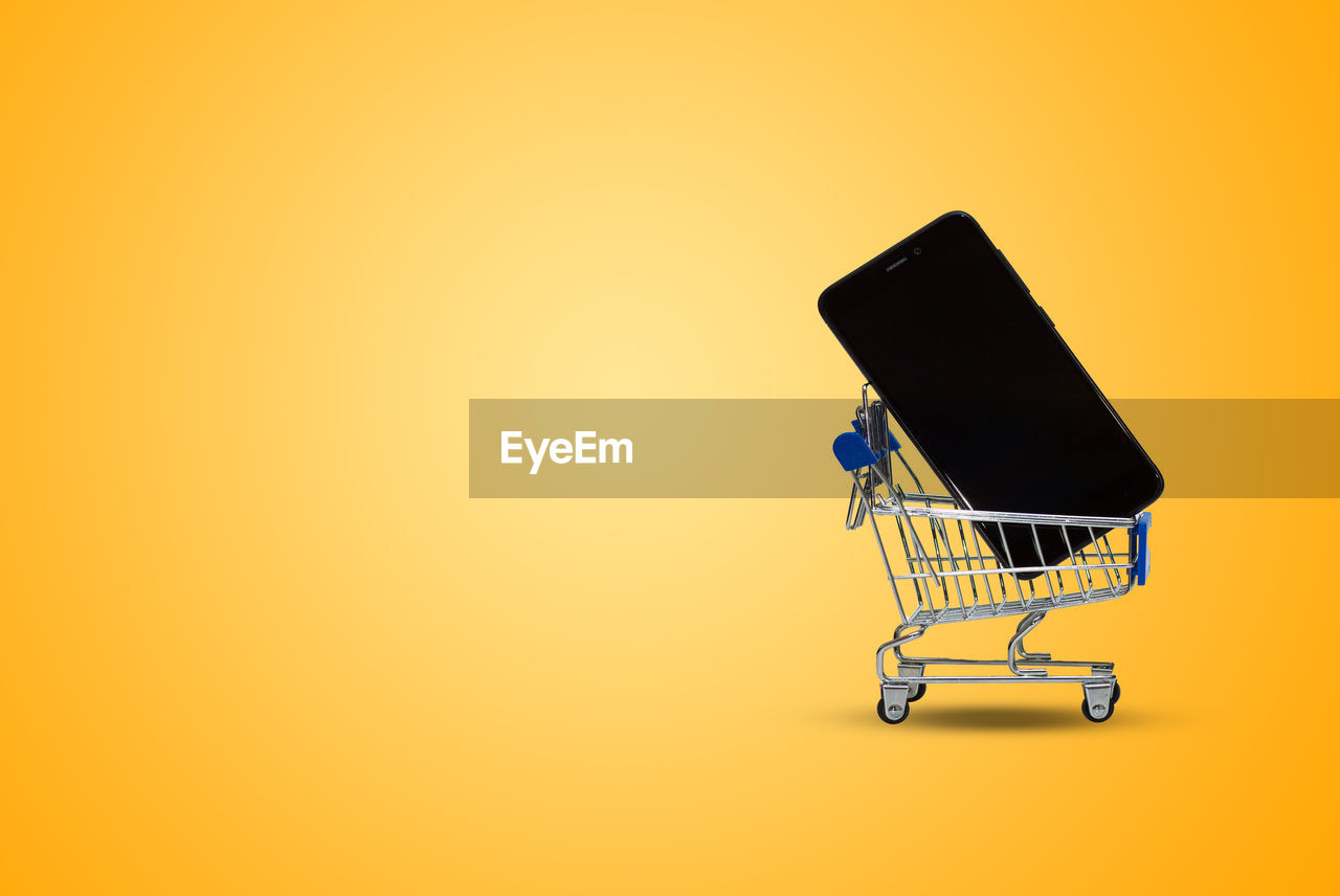 Shopping cart and a phone on yellow background, gifts online in store