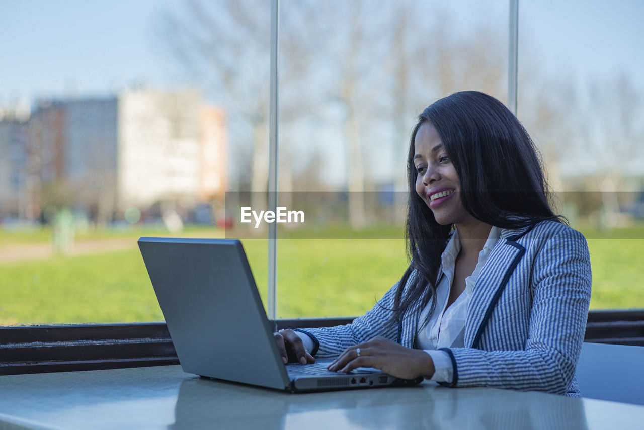 Smiling businesswoman using laptop by window in office