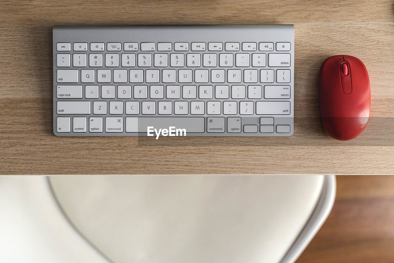 Overhead view of a table with a white keyboard and a red mouse.