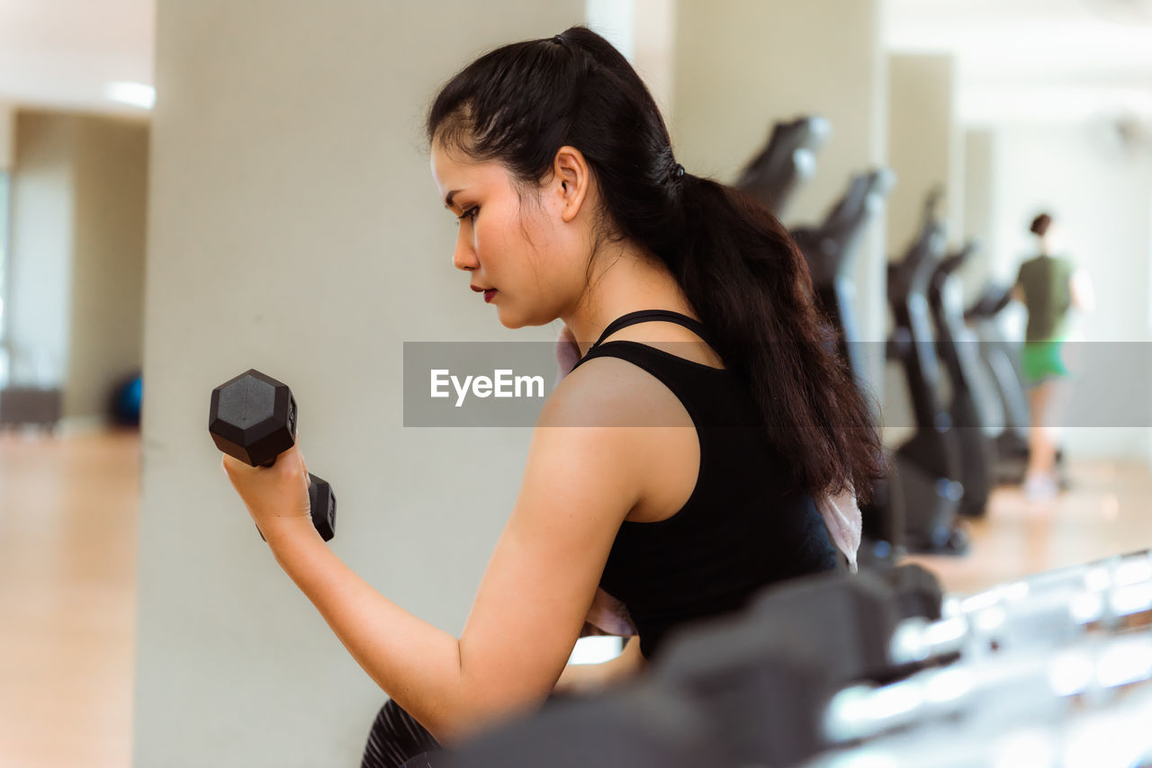 Side view of young woman exercising with dumbbell in gym