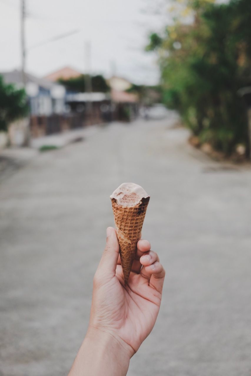 Cropped hand holding ice cream cone on street