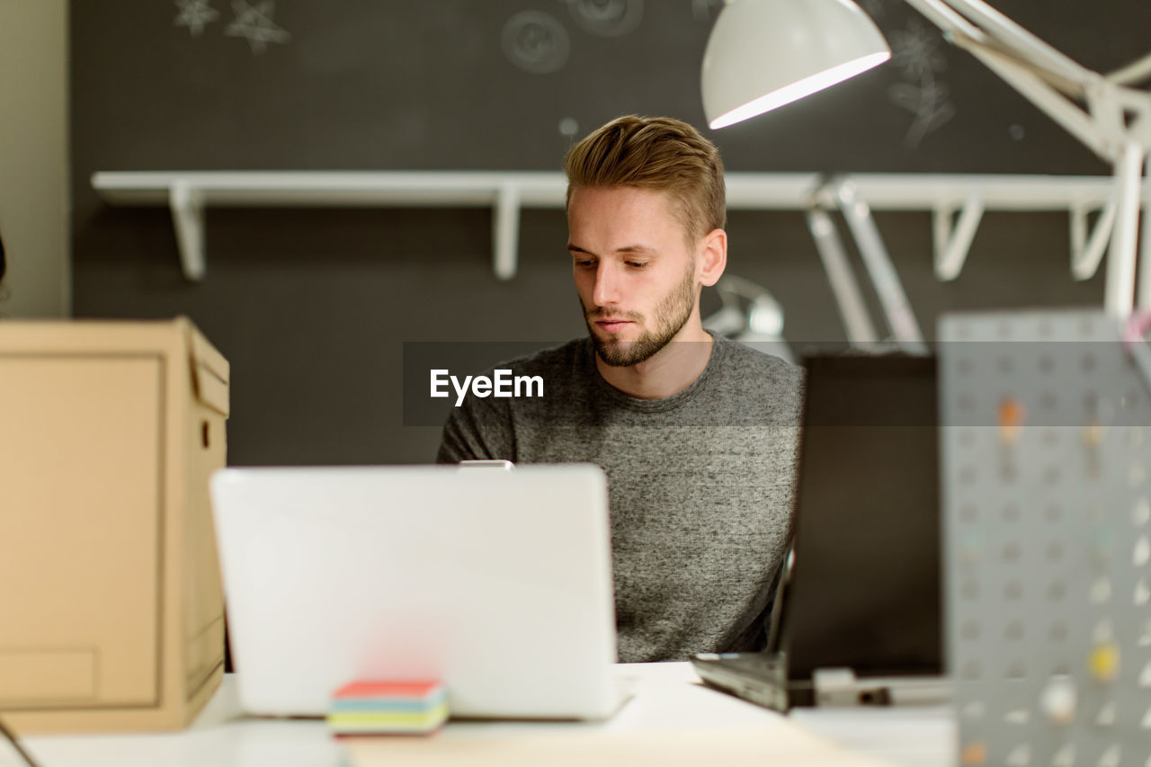 Confident young businessman using laptop while sitting at desk in creative office