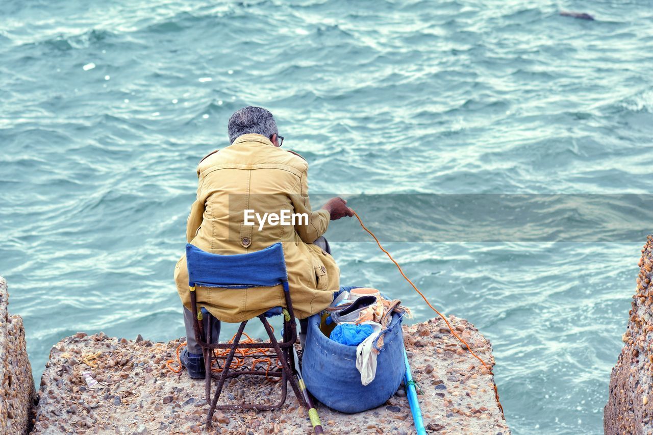 REAR VIEW OF MEN FISHING ON SEA SHORE