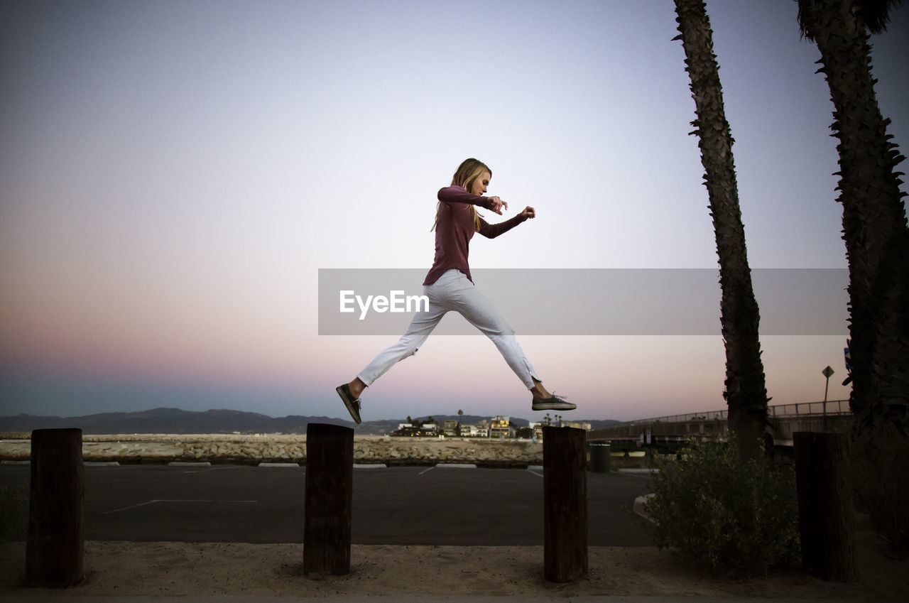 Side view of woman jumping on wooden posts in city