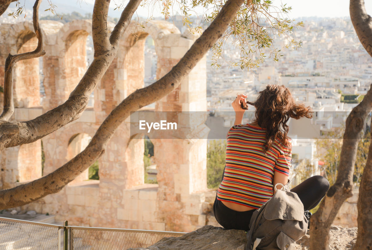 Rear view of woman sitting on branch at acropolis of athens