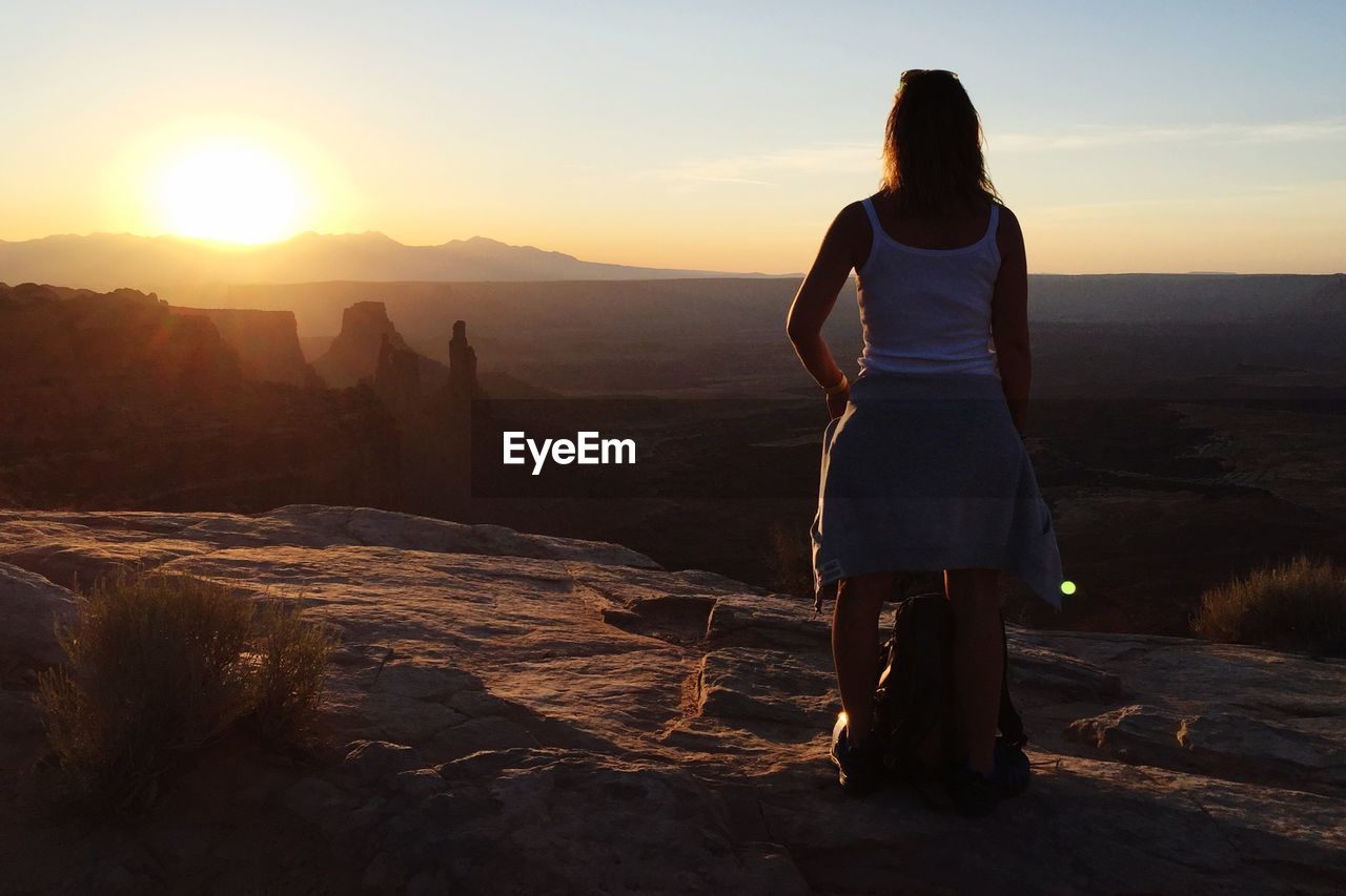 Rear view of woman standing on rock formation at sunset