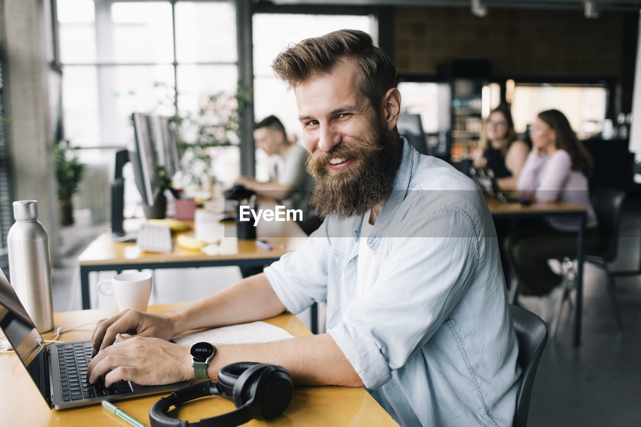 Portrait of smiling male computer programmer typing on laptop while working in office