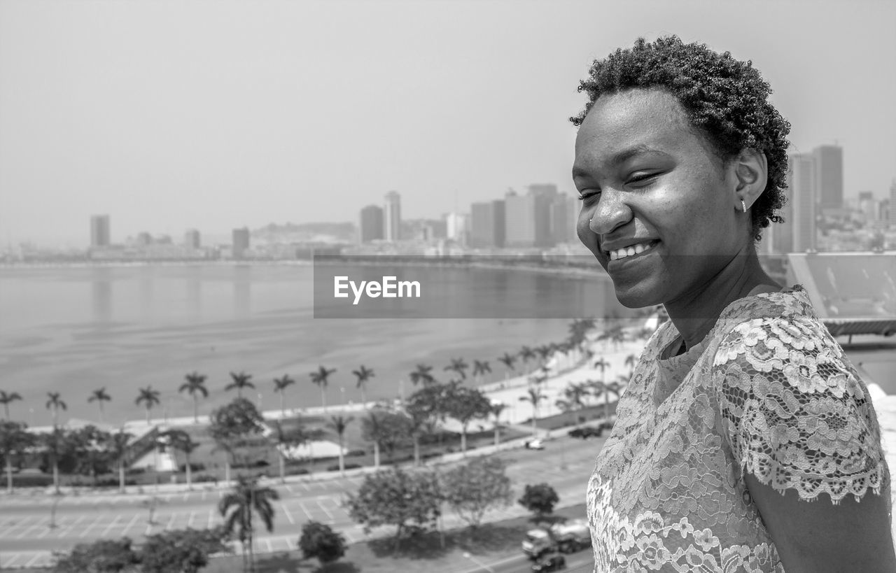 Portrait of smiling young woman in city against clear sky