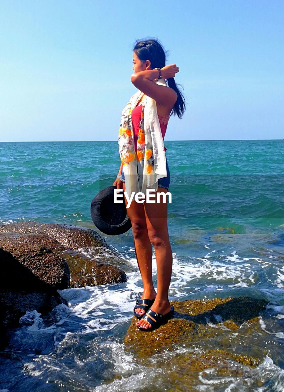 Full length of young woman standing on rock at beach