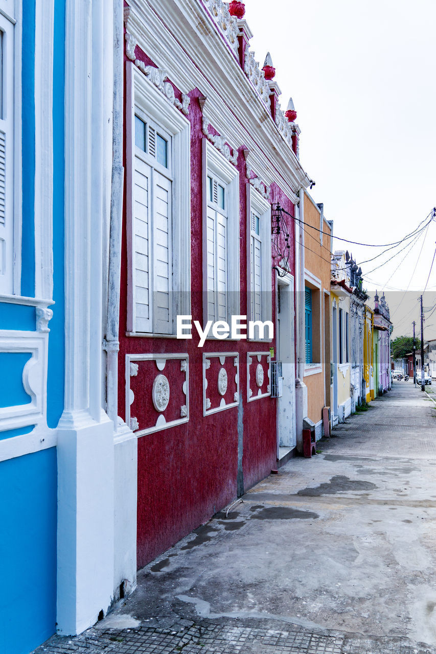 architecture, building exterior, built structure, urban area, town, street, building, city, road, no people, day, nature, facade, entrance, transportation, neighbourhood, sky, outdoors, door, residential district, transport, wall, house, footpath, red, window, in a row