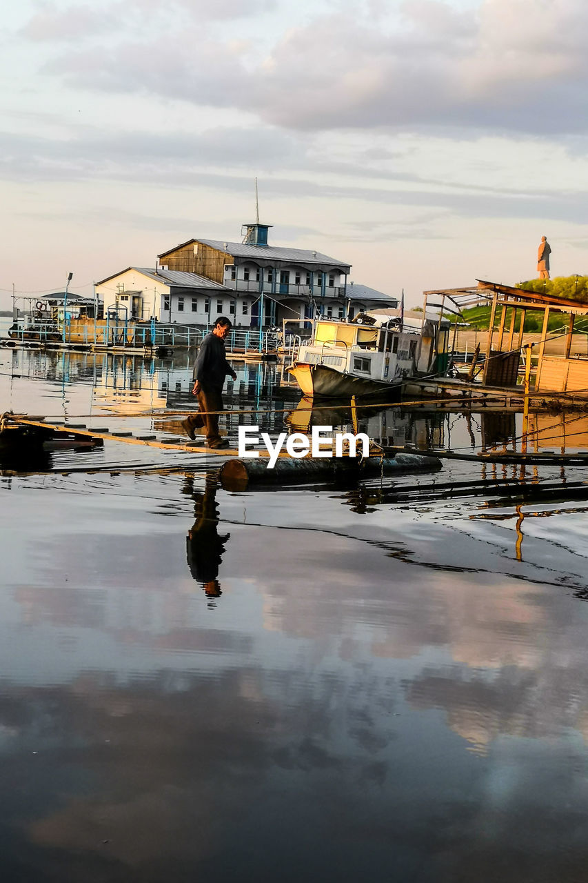 MAN STANDING IN BOAT AGAINST SKY