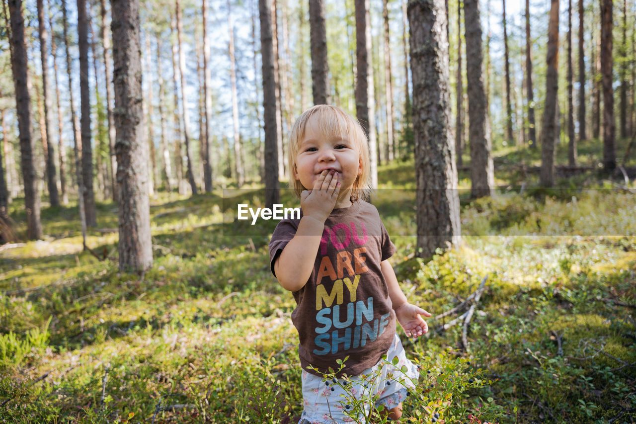 Blond baby girl picking and eating berries in the forest
