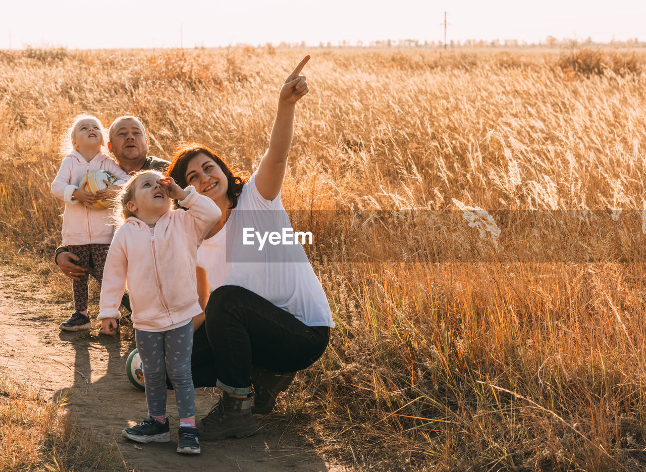 Happy family rests outdoors, indicates something interesting in sky, summer holidays, happy family