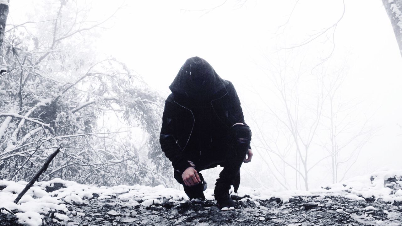 Man in hooded clothing crouching on snow covered field