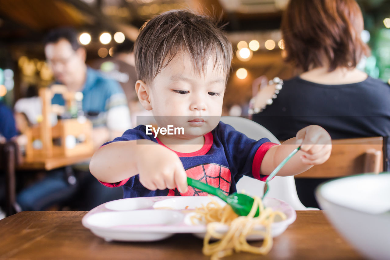 Close-up of boy eating noodles on table at restaurant