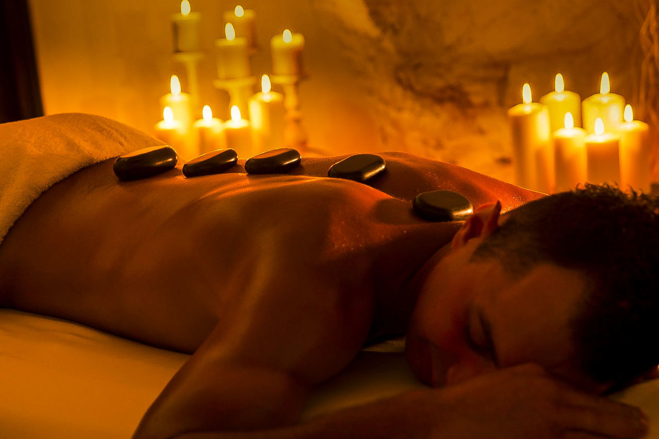 Shirtless man receiving hot stone therapy in spa