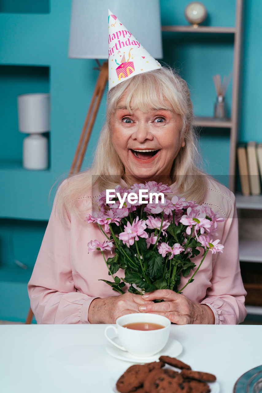 Portrait of smiling senior woman holding flowers at home