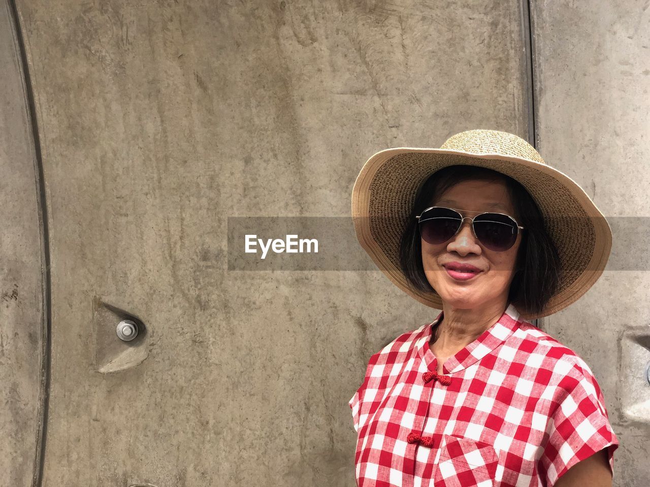 Portrait of smiling woman wearing sunglasses standing against wall
