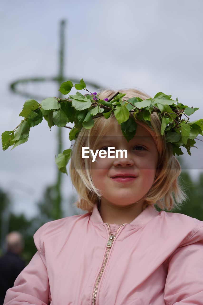 Portrait of smiling girl wearing flowers against sky