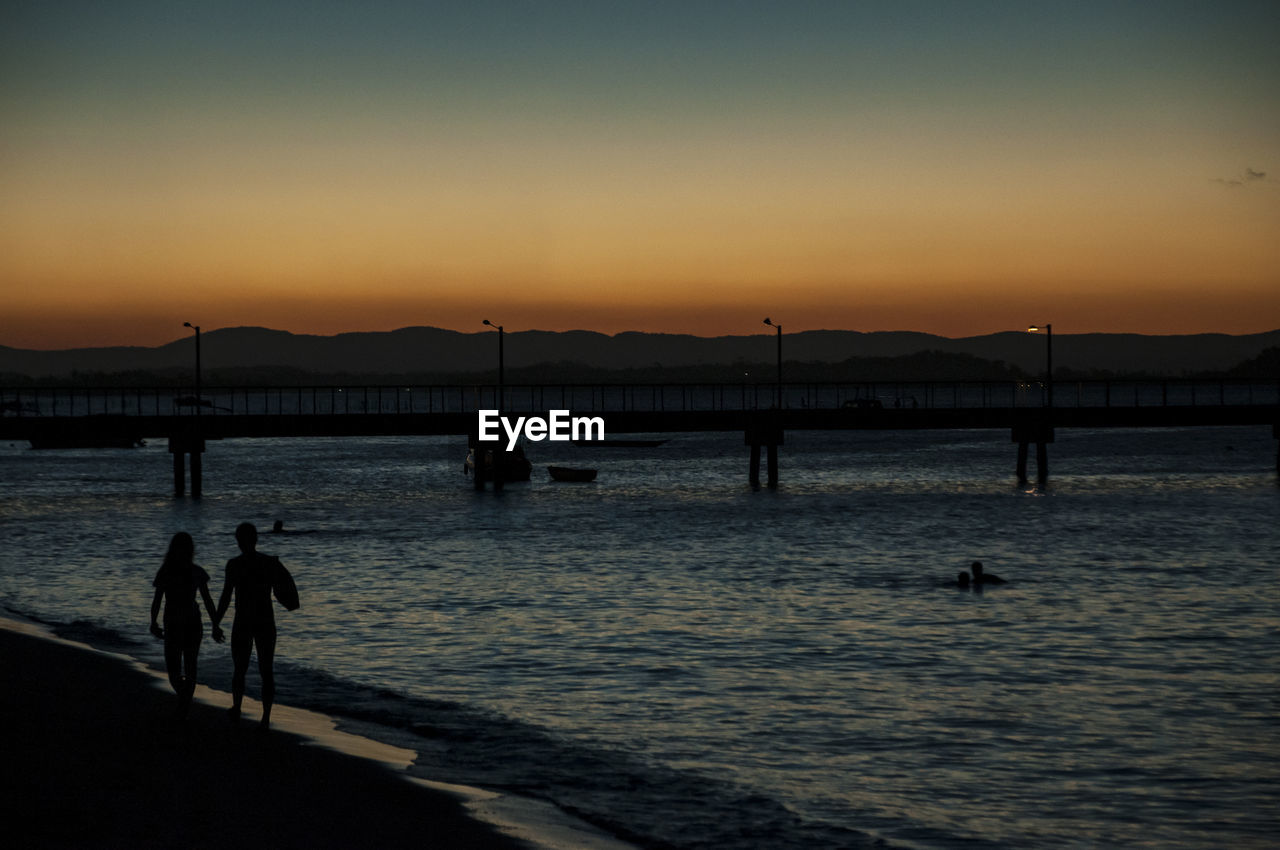 SILHOUETTE PEOPLE ON SHORE AGAINST SKY DURING SUNSET