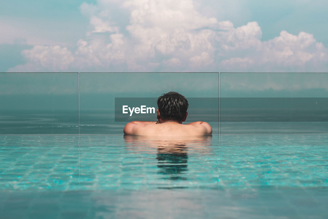 Rear view of shirtless man in infinity pool