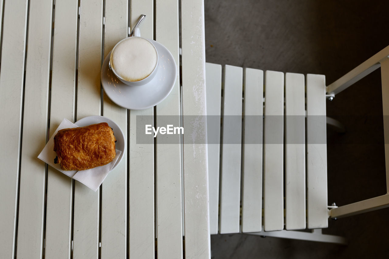 Italian cappuccino with a chocolate croissant on a white slatted table and a chair
