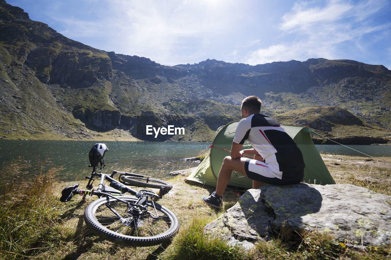 Man sitting on rock by bicycle against mountains