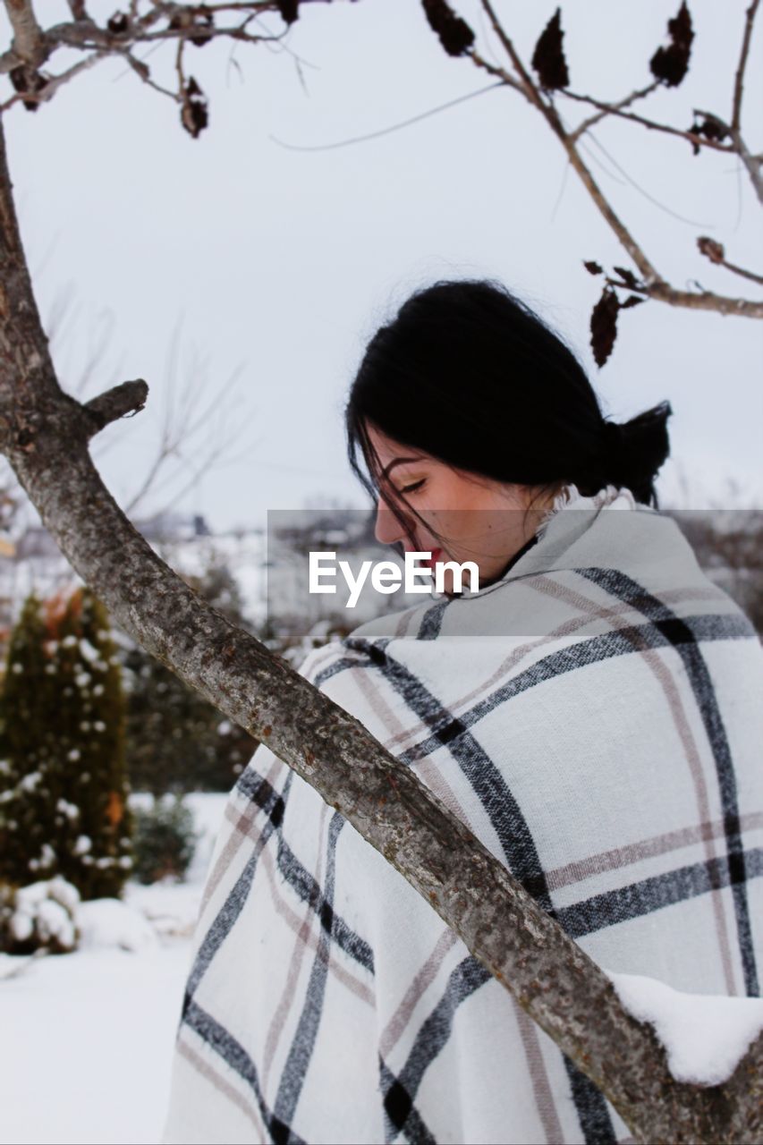 Young woman with blanket by tree during winter