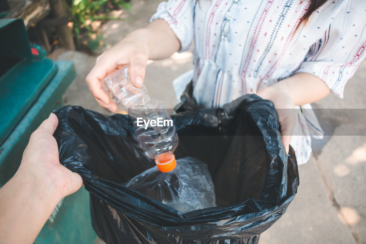 Midsection of woman putting plastic bottle in bag