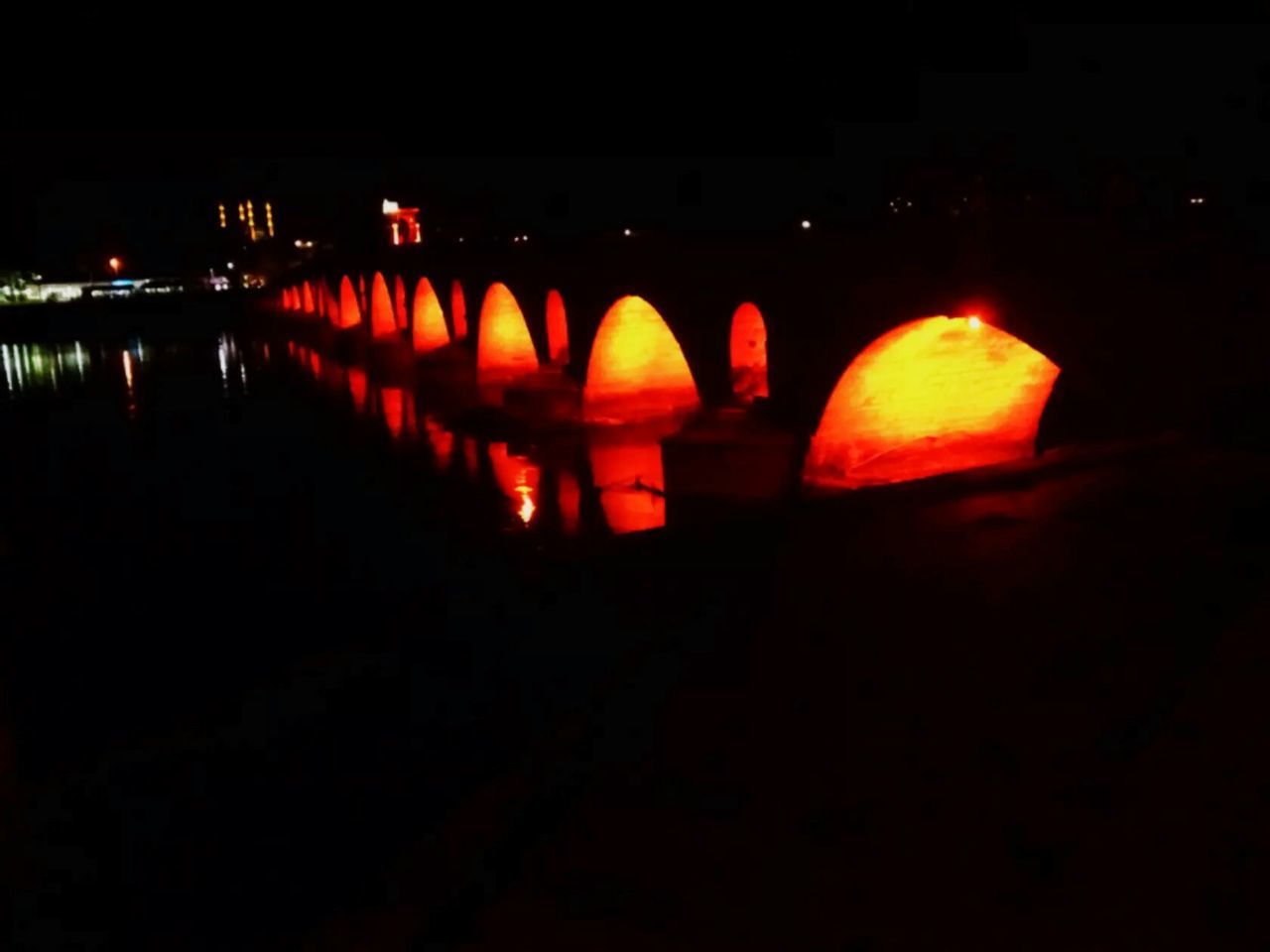 ILLUMINATED ARCH BRIDGE OVER RIVER AT NIGHT DURING SUNSET