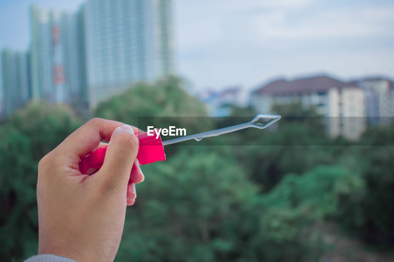 Close-up of hand holding bubble wand against building in city