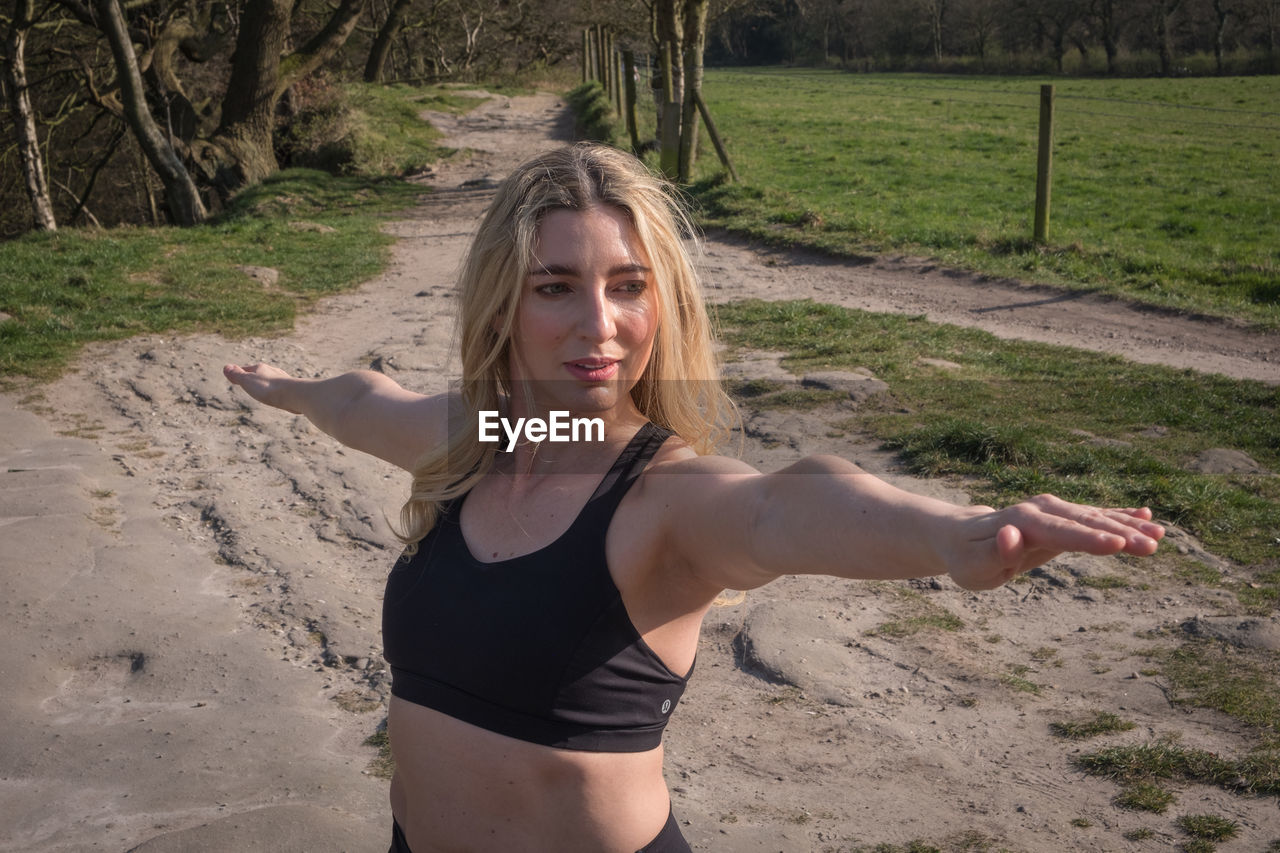 one person, women, adult, female, lifestyles, exercising, blond hair, land, young adult, nature, leisure activity, person, clothing, hairstyle, sports, portrait, sports clothing, limb, long hair, human leg, day, tree, front view, wellbeing, outdoors, looking at camera, yoga, photo shoot, standing, stretching, human face, arm, teenager, environment, smiling, vitality, relaxation, landscape, physical fitness, activity, plant, crop top