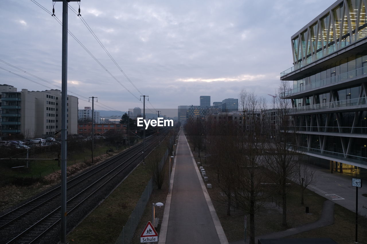 RAILROAD TRACKS BY ROAD IN CITY AGAINST SKY