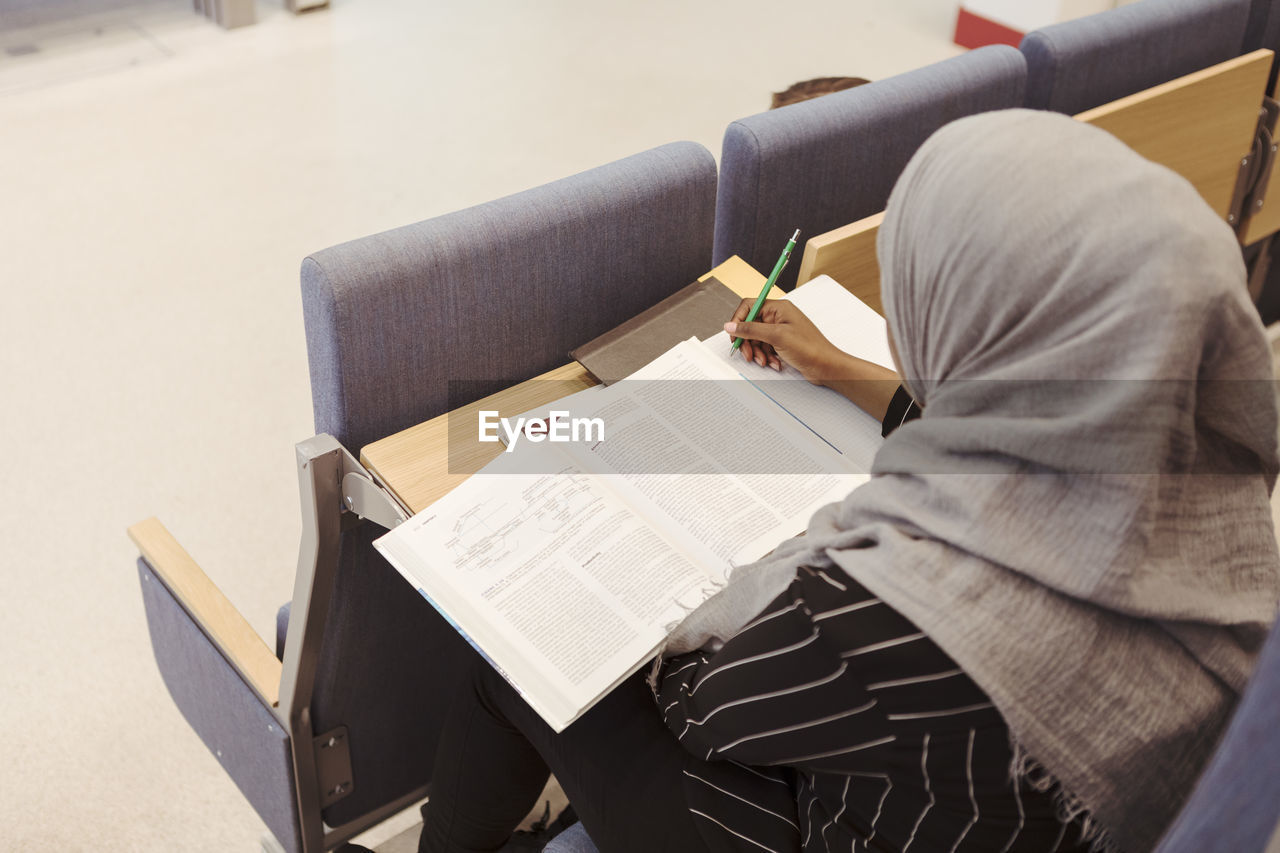 High angle view of student in hijab studying from book at lecture hall in university