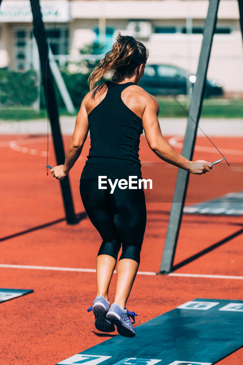 Woman jumping with rope in gym during sunny day